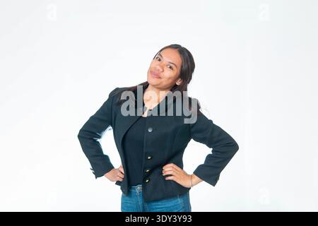 Porträt einer lächelnden indonesischen Frau, die eine schwarze strukturierte Jacke und eine blaue Jeans trägt, mit freundlichem Ausdruck in die Kamera blickt, isoliert auf weißem Rücken Stockfoto