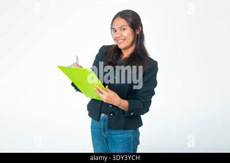 Porträt einer lächelnden indonesischen Frau, die einen gelben Blazer und ein weißes Hemd trägt, mit der Faust unter dem Kinn posiert und in die Kamera blickt, isoliert auf weiß Stockfoto