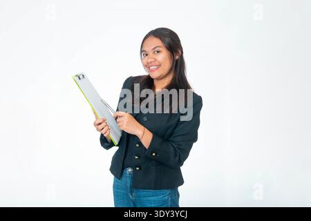 Porträt einer lächelnden indonesischen Frau, die einen gelben Blazer und ein weißes Hemd trägt, mit der Faust unter dem Kinn posiert und in die Kamera blickt, isoliert auf weiß Stockfoto