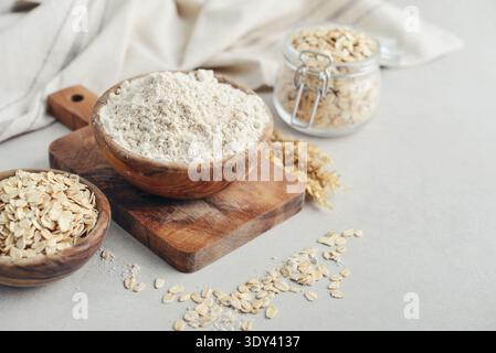 Hafermehl in Holzschüssel mit rohem Haferflocken auf hellem Hintergrund, Nahaufnahme Stockfoto
