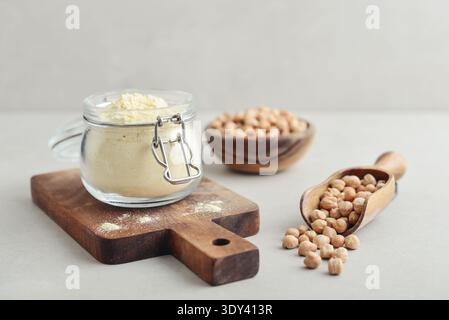 Kichererbsenmehl im Glas mit rohen Kichererbsen auf hellem Hintergrund, Nahaufnahme Stockfoto