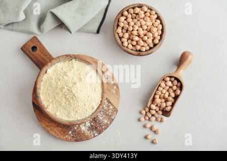 Kichererbsenmehl in Holzschüssel mit rohen Kichererbsen auf hellem Hintergrund, Nahaufnahme Stockfoto