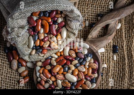 Ein hölzerner Servierlöffel und eine Schüssel sind mit einer bunten Mischung aus verschiedenen ungekochten getrockneten Bohnen und Hülsenfrüchten gefüllt. Stockfoto