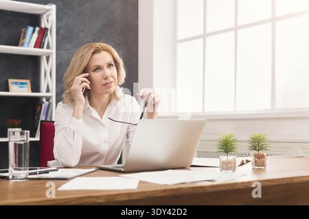 Nachdenkliche Geschäftsfrau auf der Arbeit, die am Telefon spricht Stockfoto