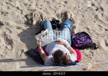 Blick von oben auf eine Frau, die am Strand von Sables d'Olonne sitzt, sich entspannt und eine Zeitschrift liest Stockfoto