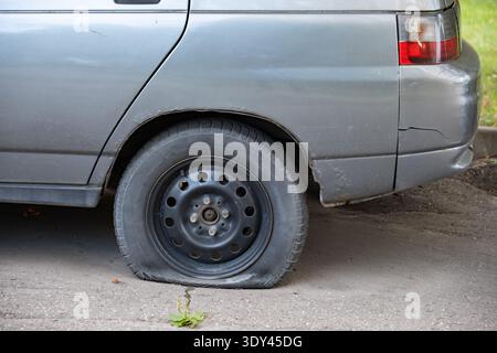 Altes graues Auto mit einem flachen, entleerten Hinterreifen auf Asphalt, das repariert werden muss Stockfoto