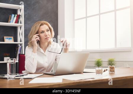 Nachdenkliche Geschäftsfrau auf der Arbeit, die am Telefon spricht Stockfoto