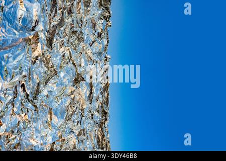 Zerknitterte Aluminiumfolie auf blauem Hintergrund, wodurch abstrakter Kopierraum entsteht Stockfoto