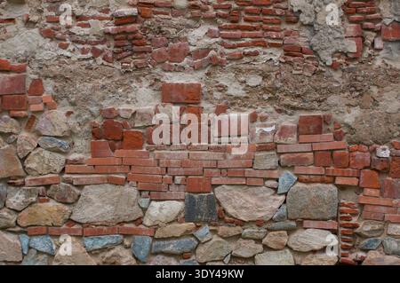 Verwitterte historische Mauer aus unregelmäßigen Steinen und roten Ziegeln mit Mörtel, die Schichten alter Mauerwerkkonstruktion und -Reparatur zeigt. Badajoz, Spanien Stockfoto