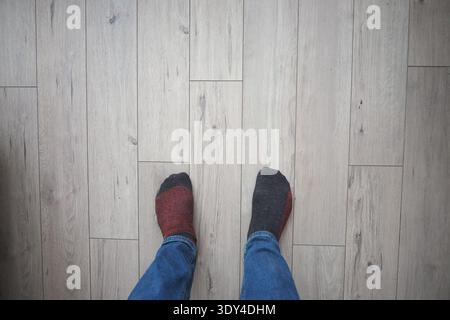 Person, die nicht passende Socken auf Holzboden trägt Stockfoto