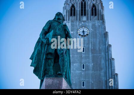 Blick auf die Bronzestatue Leif Erikson, die stolz vor der monumentalen Basaltfassade der Kirche Hallgrímskirkja in Reykjavik steht. Stockfoto