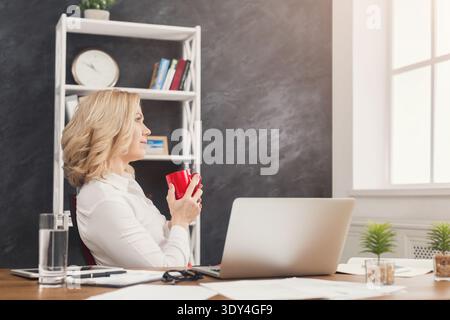 Geschäftsfrau sitzt am Arbeitsplatz mit Becher Stockfoto