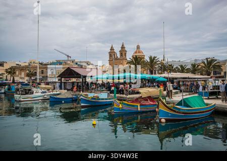 Traditionelle farbenfrohe Luzzu-Fischerboote im Hafen von Marsaxlokk mit der Pfarrkirche unserer Lieben Frau von Pompeji im Hintergrund, Malta Stockfoto