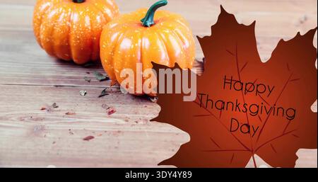 Zwei orangefarbene Mini-Kürbisse auf dem Tisch mit Ahorngrafik, die Happy Thanksgiving Day sagt Stockfoto