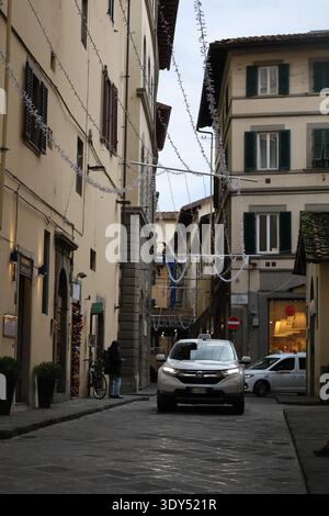 Enge Straße in Florenz mit Taxi-Auto und Weihnachtsbeleuchtung zwischen Gebäuden. Stockfoto