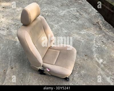 Beigefarbener Autositz aus dem Fahrzeug entfernt, im Freien auf Betonoberfläche aufgestellt. Stockfoto
