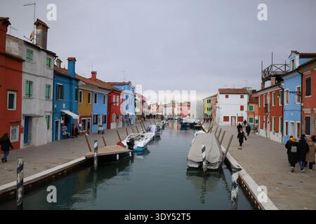 Weite Perspektive auf einen Kanal, der von farbenfrohen Häusern auf beiden Seiten gesäumt ist, mit mehreren kleinen Booten, die an der Küste angedockt sind und Menschen entlang laufen. Stockfoto