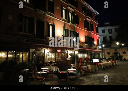 Stimmungsvolles Straßenrestaurant mit Sitzgelegenheiten im Freien und warmen Lichtern in Venedig für ein gemütliches Nachtleben. Stockfoto
