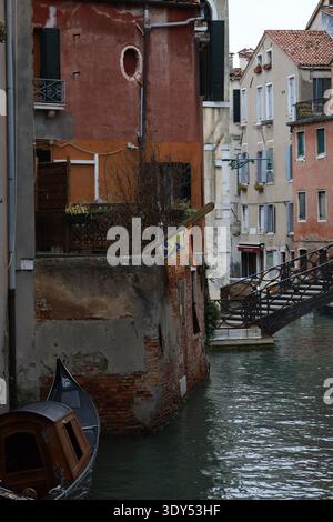 Kanalecke mit verwitterten Gebäuden, einem festgemachten Boot und einer dekorativen Brücke in einem ruhigen Viertel von Venedig. Stockfoto