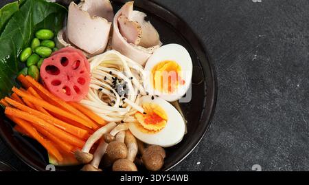 Suppe Ramen mit Rindfleisch, Gemüse und Ei in einer Schüssel auf dunklem Hintergrund. Draufsicht. Stockfoto