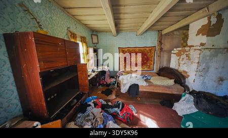 Verlassenes Zimmer mit Unordnung und unordentlichem Bett, das Verfall und Desorganisation zeigte Stockfoto