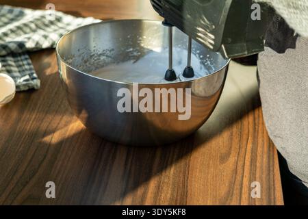 Seitenansicht des Eiweißes, das mit einem elektrischen Handmixer in einer Edelstahlschale geschlagen wird. Stockfoto