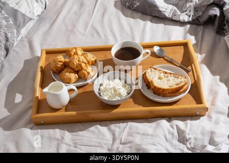 Frühstückstablett mit Kaffee, Brot, Käse und Gebäck auf einem Bett während der Morgenstunden Stockfoto