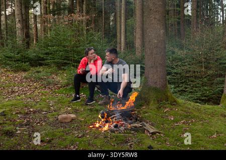 Das Paar genießt eine intime Unterhaltung am gemütlichen Lagerfeuer in einem üppigen Wald und schafft warme Erinnerungen an einen friedlichen Abend in der Natur Stockfoto