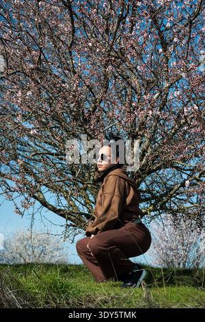 Frau in braunem Outfit und Sonnenbrille vor einem blühenden Baum Stockfoto