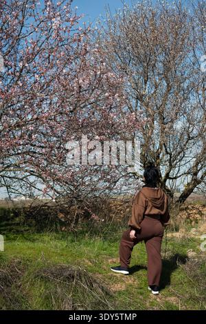 Frau, die draußen steht und blühende Mandelbäume unter blauem Himmel ansieht Stockfoto