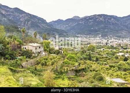 Ruhige ländliche Landschaft mit einem traditionellen Steinhaus umgeben von lebhaftem Grün und Terrassengärten mit einer Stadt im Bergtal, so Stockfoto