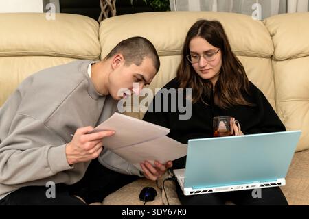 Junger Mann und Frau, die auf dem Sofa sitzen und auf den Laptop-Bildschirm schauen. Stockfoto