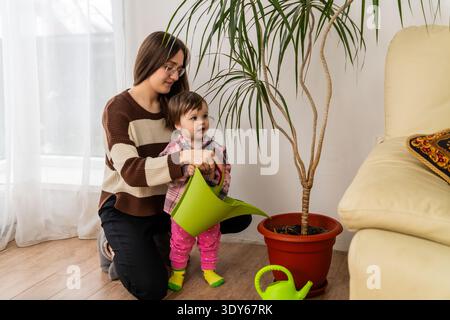 Frau und Kleinkind bewässern Zimmerpflanze mit Dose im Wohnzimmer. Stockfoto