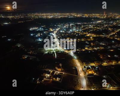 Nächtliche Luftaufnahme der Vorstadtstadt, die im Mondlicht leuchtet. Die Straßen und Häuser sind warm beleuchtet, die Straßen kurbeln sich durch Viertel. Ruhige Szene, keine Leute Stockfoto