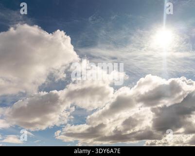 Helle Sonne scheint durch flauschige weiße Wolken gegen blauen Himmel. Wolken erzeugen weiche Schatten und erzeugen Kontrast und Tiefe. Das Bild weckt Ruhe, Hoffnung oder Stockfoto