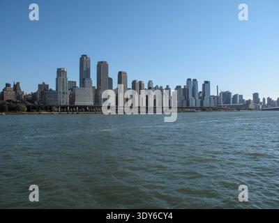 Ein Panoramablick auf Manhattan zeigt eine dichte Ansammlung von Hochhäusern, die sich hinter dem Fluss im Vordergrund erheben. Stockfoto