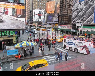 Eine geschäftige Straßenszene am Times Square zeigt große beleuchtete Plakate, starken Verkehr mit gelben Taxis und Menschenmassen von Fußgängern. Stockfoto