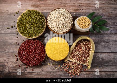 Körner und Hülsenfrüchte in Schüsseln und Körben auf hölzernem Hintergrund Stockfoto
