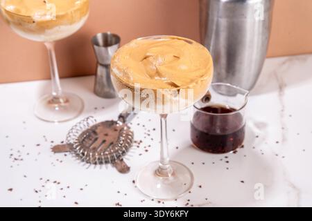 Dalgona Espresso-Martini-Cocktail mit Schlagsahne und cremigem Likör, viraler Sommercocktail in zwei Martini-Gläsern, mit Shaker und Bar-ut Stockfoto