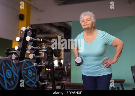 Ältere Frau trainiert Oberkörperkraft mit kleinen Gewichten während des Trainings im Fitnessstudio. Das Konzept der Seniorenfitness und des Wohlbefindens Stockfoto