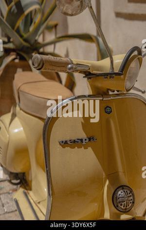 Gelbes Vespa-Moped, das in Korfu-Stadt mit Pflanzen und Gebäuden in der Nähe geparkt ist Stockfoto