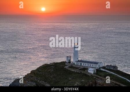 Der South Stack Lighthouse leuchtet, wenn die Sonne über dem Meer auf Holy Island in Anglesey, Nordwales, mit einem warmen Orangenschein untergeht Stockfoto