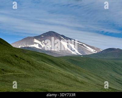 Great Sitkin Island zeigt schneebedeckte Gipfel und grüne Hügel bei klarem Wetter in Alaska Stockfoto