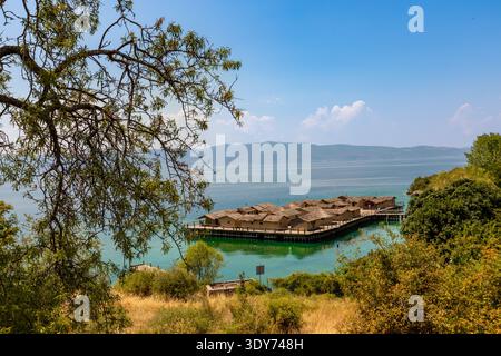 Blick auf das Stelzendorf mit Strohhütten über türkisfarbenem Wasser und Berge in der Ferne in Ohrid, Mazedonien Stockfoto