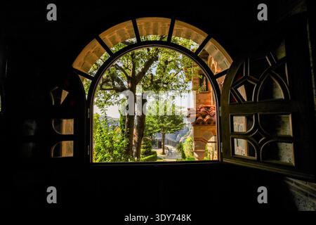 Malerischer Blick durch ein großes bogenförmiges Holzfenster, das einen Innenhof und Berge in Griechenlands Meteora-Region zeigt Stockfoto