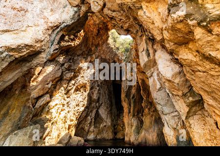 Erkunden Sie einen Felsbogen und eine Meereshöhle mit Sonnenlicht, das auf Steinmauern in Albanien in der Nähe von Dhermi am Ionischen Meer strahlt Stockfoto