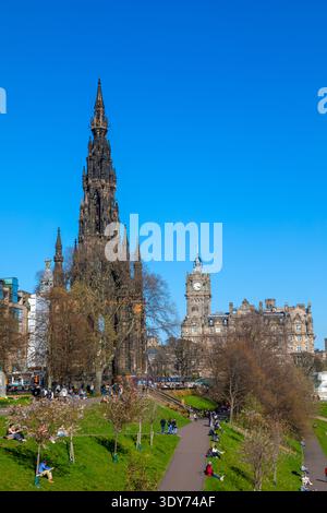 Die Sonne scheint auf Sir Walter Scott Monument und Balmoral Hotel, während die Leute die Princes Street Gardens in Edinburgh genießen Stockfoto