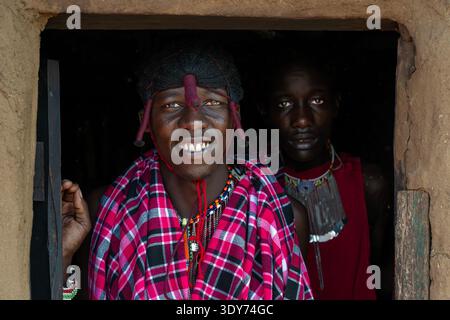 Zwei Maasai-Stammesleute in traditioneller Kleidung stehen in der Tür des Schlammhauses in Maasai Mara Kenia Stockfoto