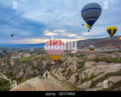 Touristen beobachten, wie Heißluftballons bei Sonnenaufgang über Kappadokien aufsteigen und dabei den Blick auf die Landschaft genießen Stockfoto
