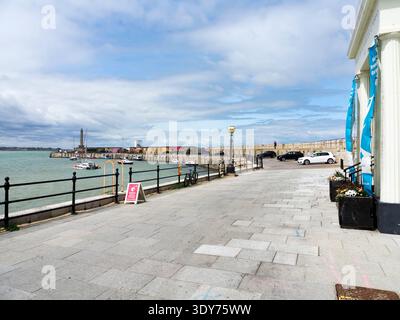 Besucher spazieren entlang des Margate Harbour Arm mit Booten, die an einem bewölkten Tag in Kent im Wasser verankert sind Stockfoto